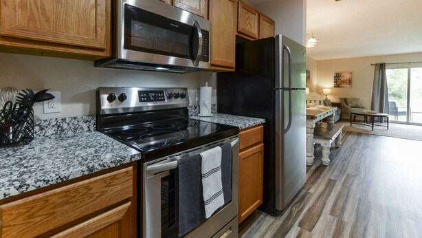 A modern kitchen with wooden cabinets, stainless steel appliances, granite countertops, and a view to the living area. - Nature's Hold - Open Pool! Central Location! Natural Views! Cozy & elegant feel! (Branson)