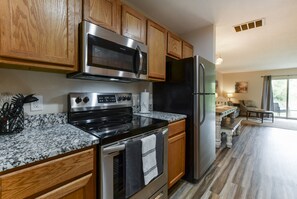 A modern kitchen with wooden cabinets, stainless steel appliances, granite countertops, and a view to the living area. - Nature's Hold - Open Pool! Central Location! Natural Views! Cozy & elegant feel! (Branson)