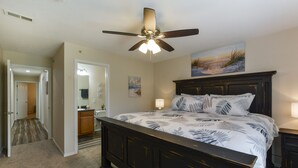 A bedroom with a dark wooden bed, a ceiling fan, a painting on the wall, and a hallway leading to another room. - Nature's Hold - Open Pool! Central Location! Natural Views! Cozy & elegant feel! (Branson)