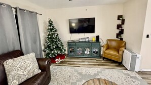 A living room with a brown leather sofa, a Christmas tree, a television, and a brown leather armchair. - Nature's Hold - Open Pool! Central Location! Natural Views! Cozy & elegant feel! (Branson)