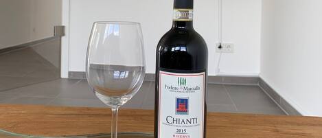 A bottle of Chianti wine and a wine glass on a glass table in a room with a television mounted on the wall.