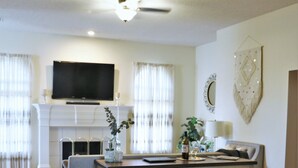 Ein modernes Wohnzimmer mit Essbereich, Kamin und flach an der Wand befestigtem Fernseher.