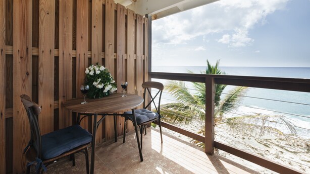 Een houten terras met een tafel en stoelen, met uitzicht op een strand.