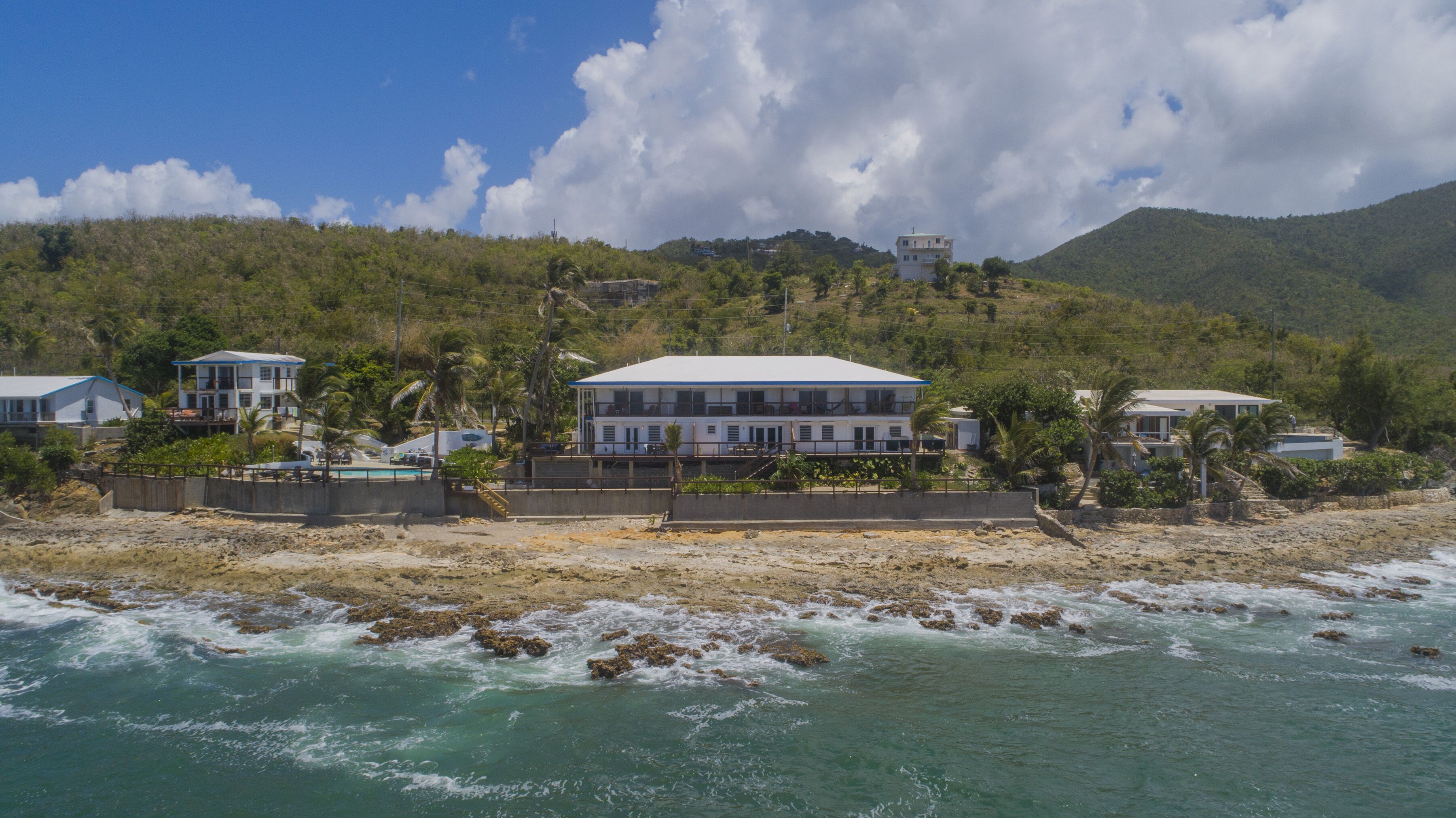A beachfront property with multiple houses, a swimming pool, and a rocky shoreline.