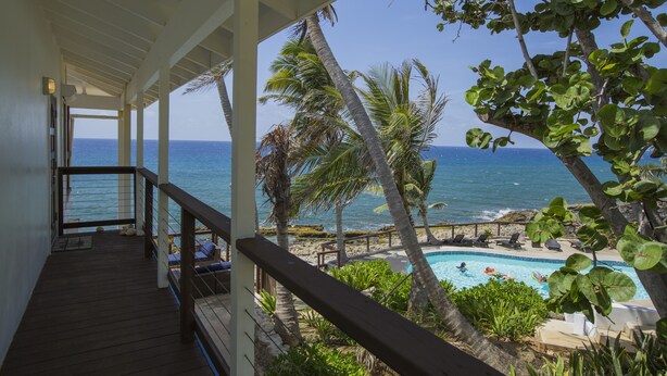 A wooden deck with a railing overlooking a swimming pool and the ocean.