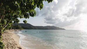A beach with clear water, people swimming, and mountains in the background.