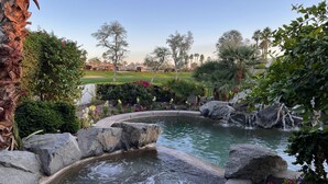 Un jardin paisible avec un étang, entouré d’une végétation luxuriante et de gros rochers.