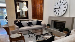 Un salon moderne avec un ensemble de canapés, une table basse en verre et une grande horloge murale.