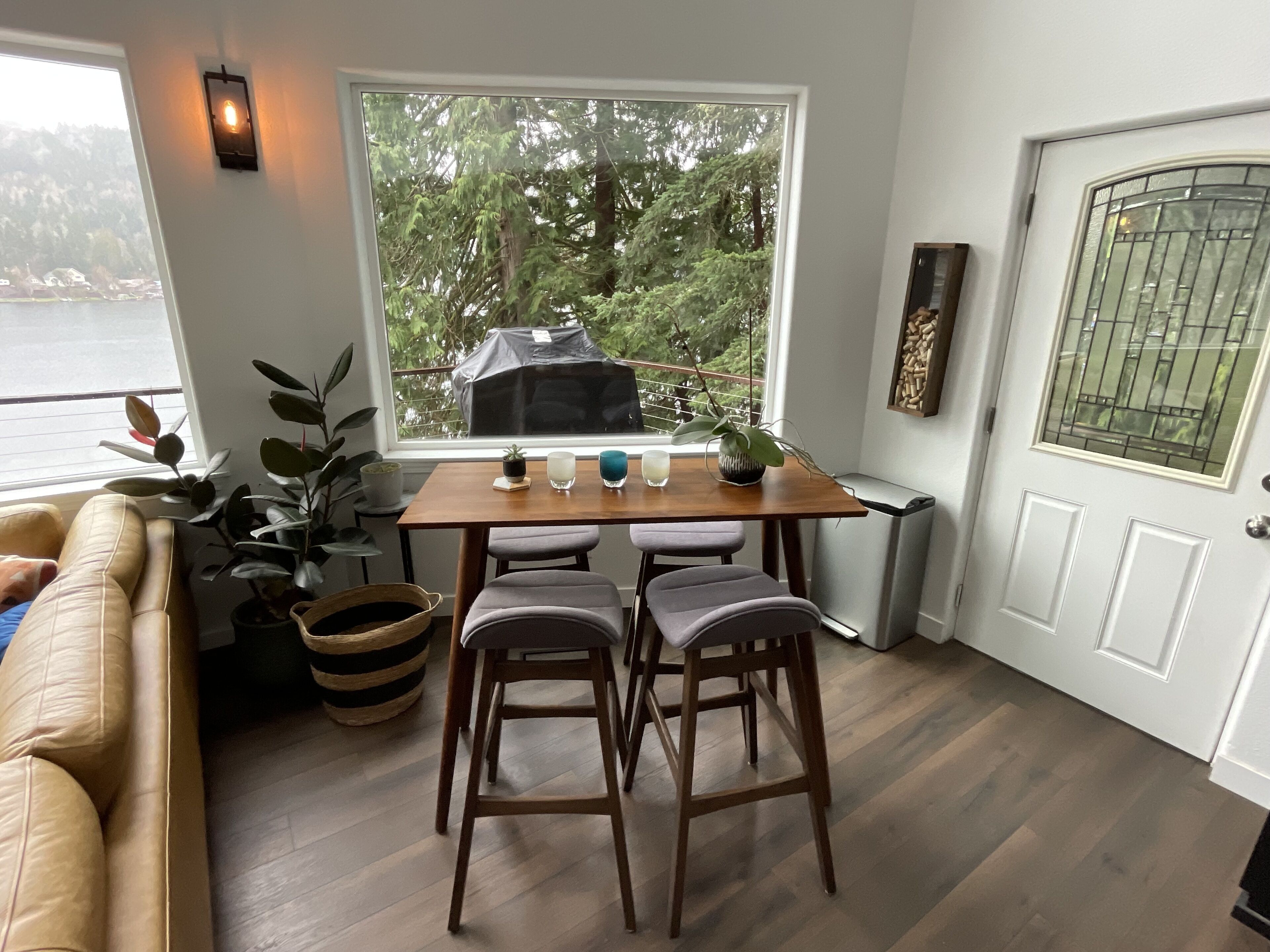 Une pièce chaleureuse avec une table en bois, deux chaises, un banc rembourré et une grande fenêtre donnant sur des arbres et une étendue d’eau.