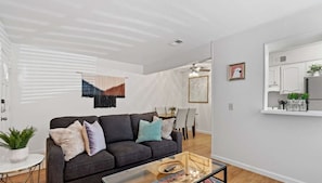 A modern living room with a dark grey sofa, a glass coffee table, and a dining area with a white table and chairs. - Nice ‘n’ Quiet Downtown Apt, Pool + Free Parking (Austin)