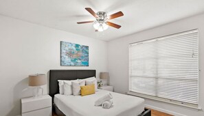 A bedroom with a bed, bedside tables, a ceiling fan, a window with blinds, and a painting on the wall. - Nice ‘n’ Quiet Downtown Apt, Pool + Free Parking (Austin)