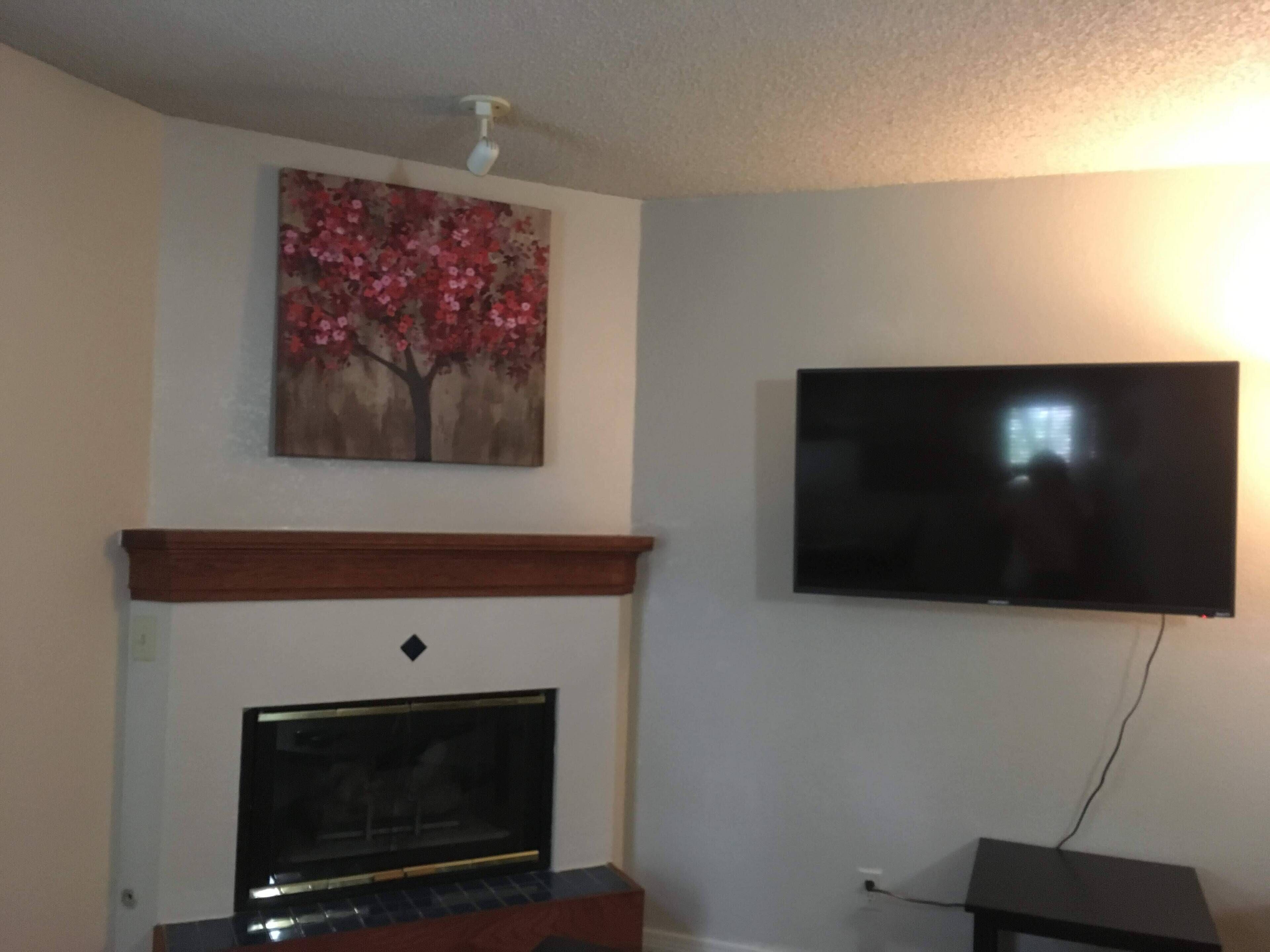 A living room with a fireplace, a mounted flat-screen TV, and a floral artwork above the fireplace.