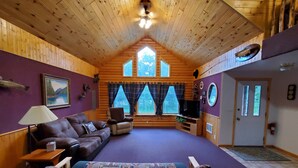 Een blokhut interieur met een groot bed, een bank, een televisie en een open haard.