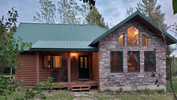 Een chalet met een stenen buitenkant en een groen dak, met een veranda met zitplaatsen en een zichtbaar interieur.