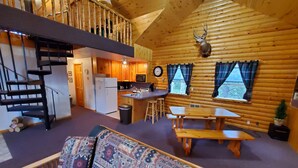 Een gezellig blokhutinterieur met een houten trap, een keuken, een eethoek en een woonkamer met een gestreept bankje.