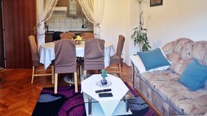 A cozy living room with a sofa, a dining table with chairs, a small table with a plant, and a kitchen in the background. - Holiday apartment mit Klimaanlage und Terrasse (Starigrad-Paklenica)