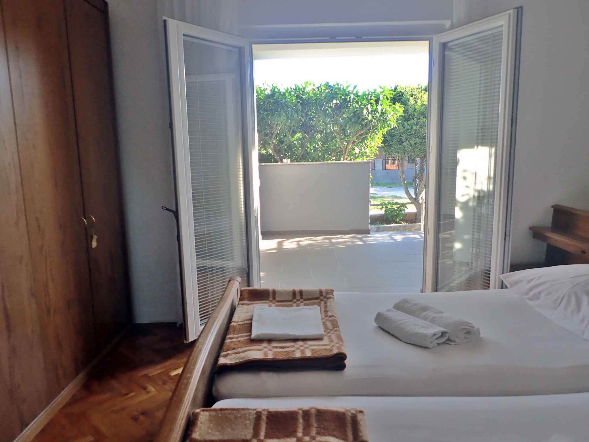 A hotel room with a bed, a wooden wardrobe, and a view of a garden through open sliding doors.