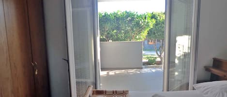 A hotel room with a bed, a wooden wardrobe, and a view of a garden through open sliding doors.