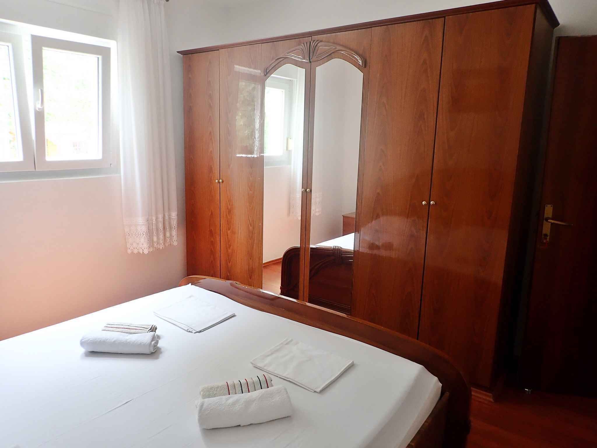 Une chambre avec une armoire en bois, un lit avec du linge de lit blanc et une fenêtre avec des rideaux.