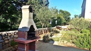 A stone barbecue grill with a chimney, set in a garden with a stone wall and greenery. - Holiday apartment mit Klimaanlage und Terrasse (Starigrad-Paklenica)