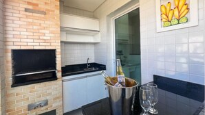 A kitchen with a brick oven, white tiled backsplash, a black countertop, and a glass door leading to a bathroom. - EXCELLENT APARTMENT 47 - with sea view, absolute hygiene, we have other options. (Ubatuba)