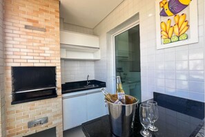 A kitchen with a brick oven, white tiled backsplash, a black countertop, and a glass door leading to a bathroom.