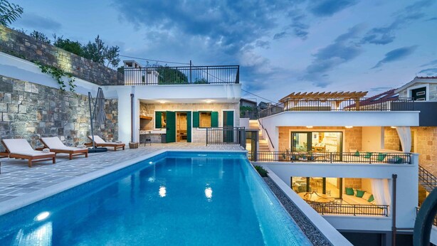 A swimming pool with lounge chairs, a stone wall, and a building with a balcony and outdoor seating area. - Beautiful private villa for 12 people with A/C, private pool, WIFI, hot tub, TV and terrace (Solin)