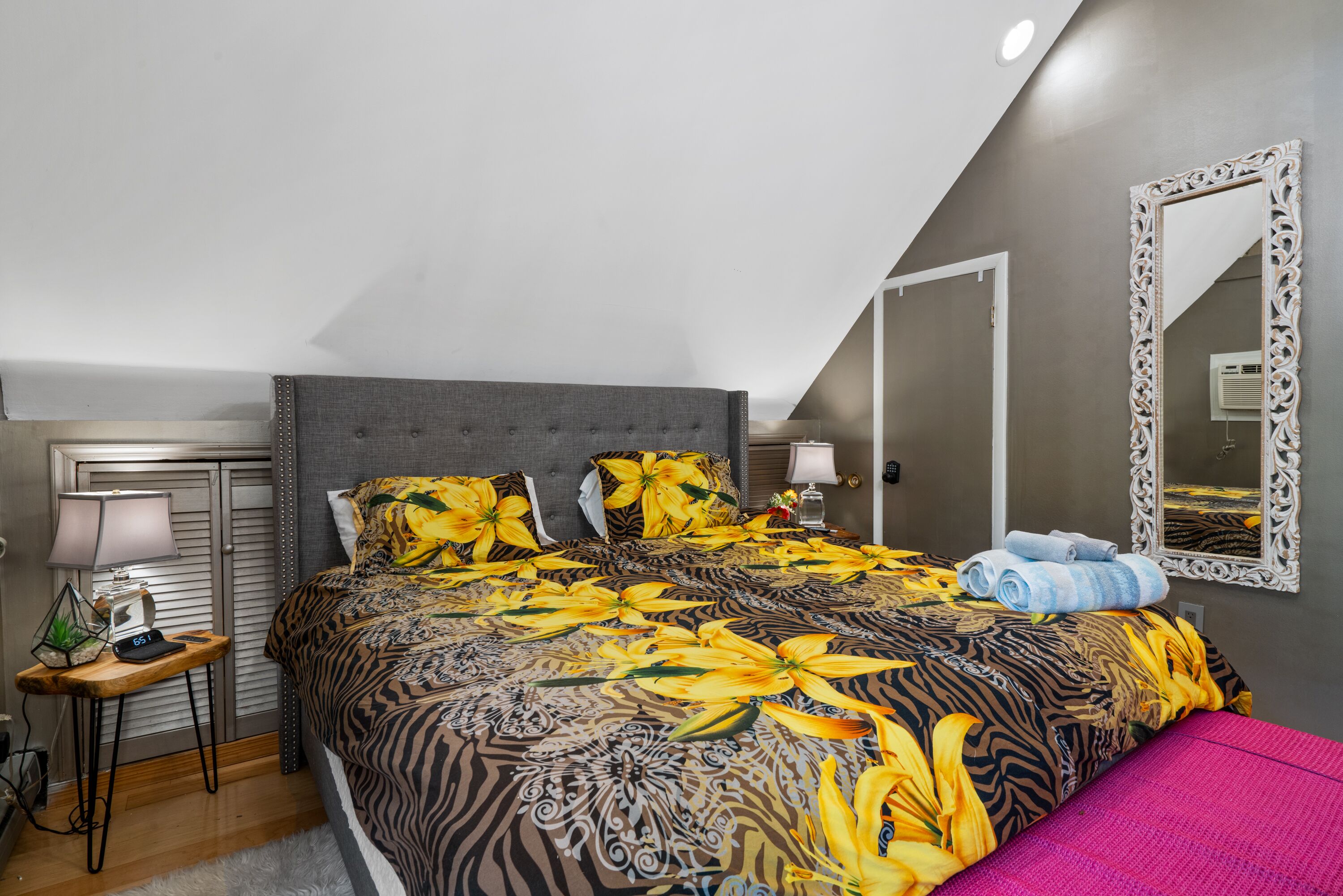 A bedroom with a bed, a nightstand, a lamp, and a mirror.