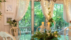 A dining table with a glass top, surrounded by white chairs, set with candles and floral arrangements.