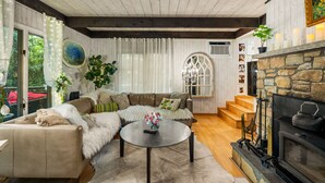 A cozy living room with a fireplace, a sofa, a coffee table, and a staircase leading to a loft area.