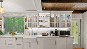 A modern kitchen with white cabinets, a built-in microwave, and a window with a forest view.