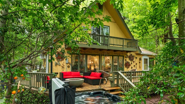 A cozy cabin with a hot tub, red outdoor furniture, and a balcony overlooking a lush garden.