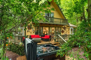 A cozy cabin with a hot tub, red outdoor furniture, and a balcony overlooking a lush garden. - Lake Naomi Forest Oasis Retreat with Hot Tub & Lounging Galore (Pocono Pines)