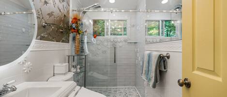 A modern bathroom with a shower, toilet, sink, and a large mirror.