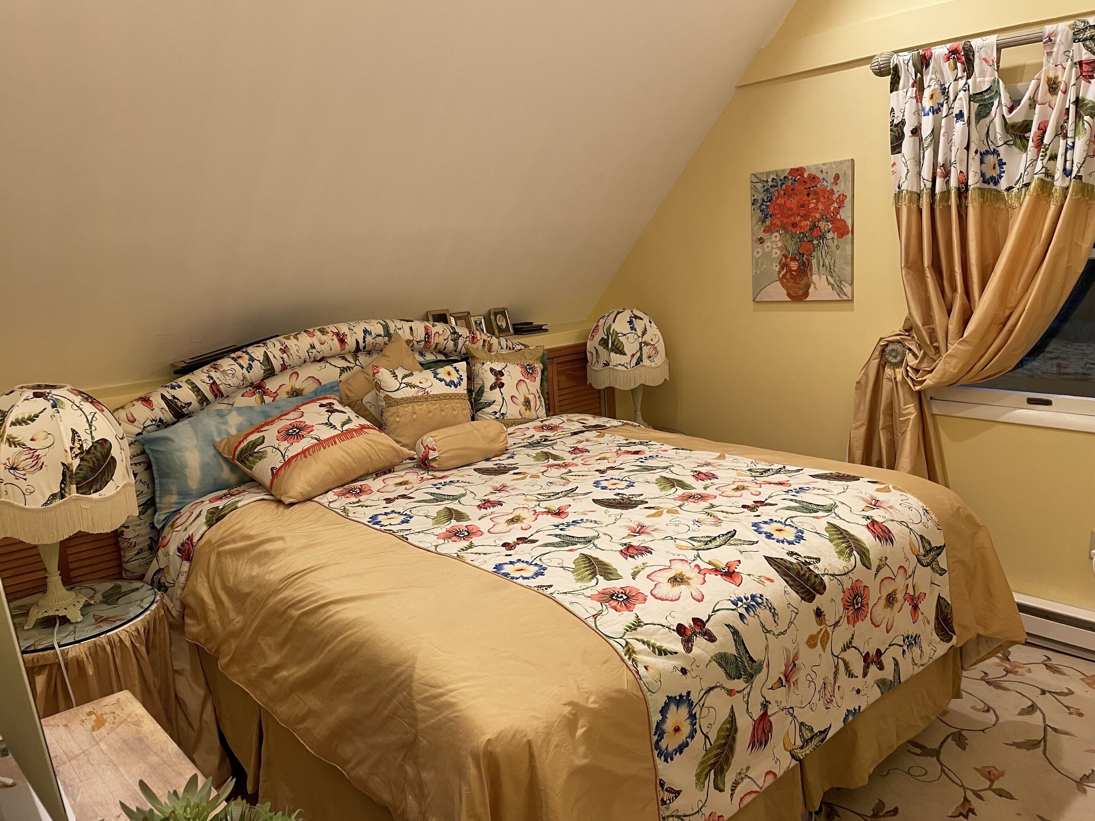 Een slaapkamer met een bloemenprint sprei, een houten hoofdbord en een raam met gordijnen.