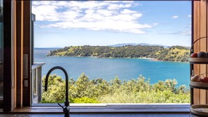 A kitchen with a view of a lake and hills. - Designer living with stunning views across the bay, a spa and coast walks. (Waiheke Island)
