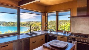 A modern kitchen with large windows offering a scenic view of a coastal landscape. - Designer living with stunning views across the bay, a spa and coast walks. (Waiheke Island)