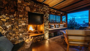 A stone fireplace with a TV, a stone wall, and a wooden ceiling. - Designer living with stunning views across the bay, a spa and coast walks. (Waiheke Island)