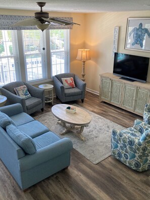 Ein Wohnzimmer mit einer Couch, Sesseln, einem Couchtisch, einem Fernseher und einem Kamin.
