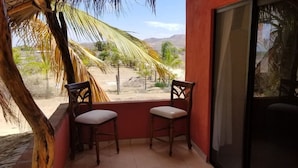 A balcony with two wooden chairs and a view of a desert landscape with palm trees. - Las Palmas (Ejido Plutarco Elias Calles)