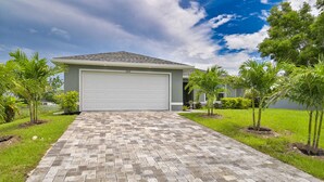 A residential garage with a paved driveway leading to a house. - Modern Coastal 3 Bedroom Villa with Salt Water Heated Pool & Office! (Cape Coral)