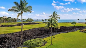 Campo de golf con palmeras, cielo despejado y vista al océano.