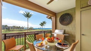 Un balcón con una mesa de vidrio dispuesta para el desayuno, sillas de mimbre, vista al océano y una pared de ladrillo con un plato decorativo.