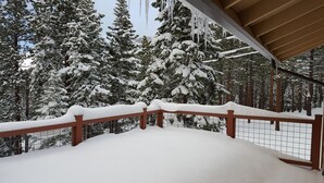 Un balcón cubierto de nieve con barandilla de madera, con vistas a un bosque de árboles cargados de nieve.