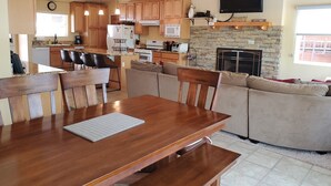 Una cocina moderna con armarios de madera, un comedor con mesa y sillas de madera, una chimenea de piedra y un televisor de pantalla plana montado en la pared.