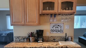 Una cocina con armarios de madera, encimera de granito, cafetera y espacio para vinos.
