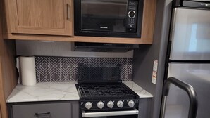 Une cuisine compacte équipée d’un four à micro-ondes encastré, d’une cuisinière et d’un évier en acier inoxydable.