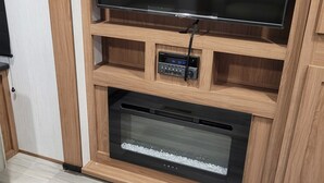 Un meuble de rangement en bois pour appareils multimédias, doté d’un téléviseur à écran plat, d’une horloge numérique et d’une barre de son intégrée.