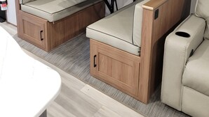 Un intérieur de camping-car compact comprenant un coin cuisine, un espace repas et un coin salon avec une table et des banquettes rembourrées.