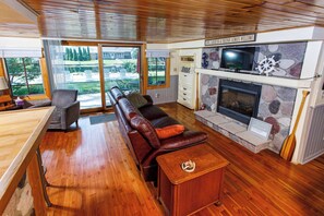Una sala de estar con piso de madera, sofá de cuero, televisor, chimenea de piedra y un cartel sobre la chimenea.